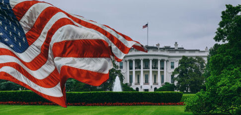 American flag waves before the White House on a cloudy day