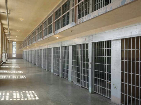 Empty prison cell block with barred doors and walkway.