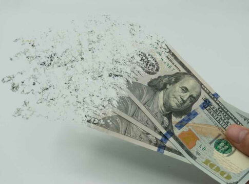 Hand holding dissolving one hundred dollar bills, Benjamin Franklin.