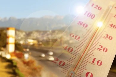 Close-up of a thermometer in hot sun over a blurred road and mountains