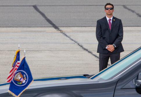 A security guard in a suit stands near a presidential vehicle at an airport