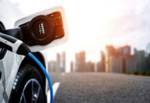 EV Values COLLAPSE, Range Barely Budges Electric car charging with city skyline background.