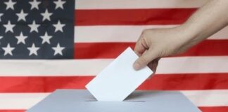 Hand casting ballot into box before U.S. flag