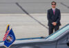 A security guard in a suit stands near a presidential vehicle at an airport
